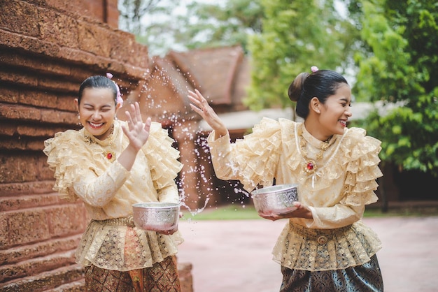 Free photo young smiling women dress in beautiful thai costumes splashing water in temples and preserve the good culture of thai people during songkran festival thai new year family day in april