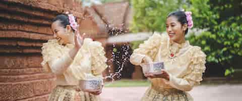 無料写真 若い笑顔の女性は、寺院で水をはねかける美しいタイの衣装を着て、4月のソンクラン祭りタイ新年家族の日にタイの人々の良い文化を維持します