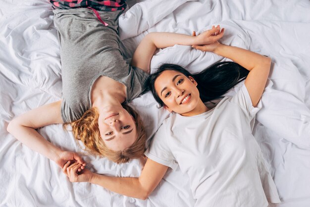 Young smiling women lying in bed and holding hands