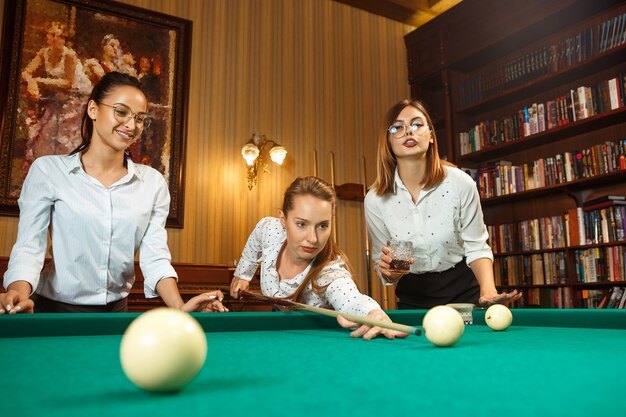 Young smiling women playing billiards at office or home after work. Business colleagues involving in recreational activity. Friendship, leisure activity, game concept.