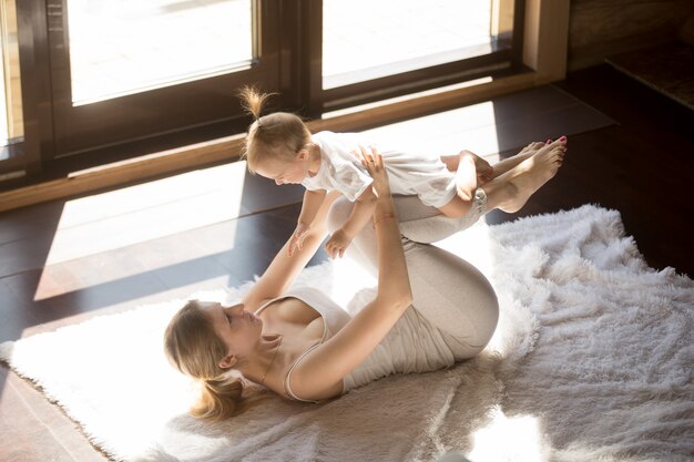 Young smiling yogi mother and baby daughter exercising at home