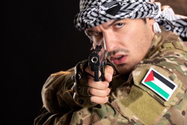 Young soldier in camouflage fighting with gun on dark wall