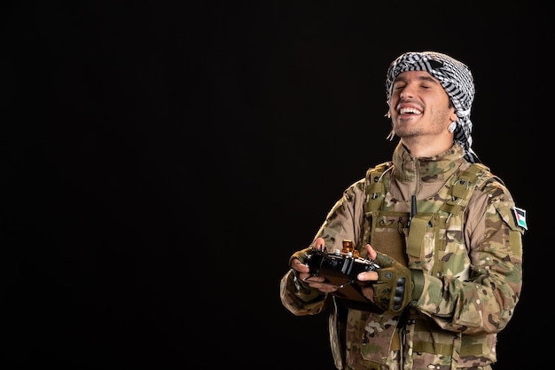 Young soldier in camouflage using remote controller on black wall