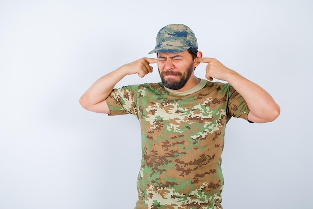 Free photo young soldier is closing eyes and covering ear with forefingers on white background