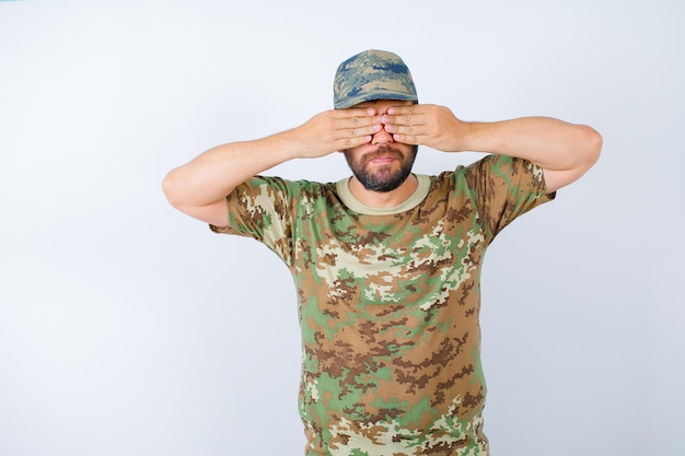 Free photo young soldier is covering his eyes with hands on white background