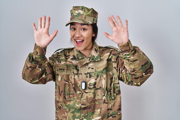 Young south asian woman wearing camouflage army uniform showing and pointing up with fingers number ten while smiling confident and happy.