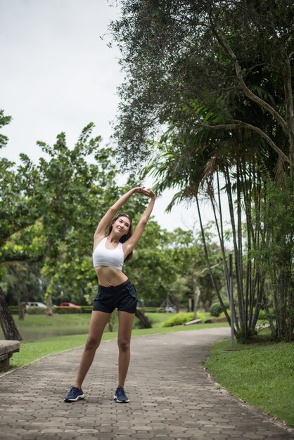 若いスポーツ女性ランナーは、公園でトラックを走る前に体を伸ばしています。