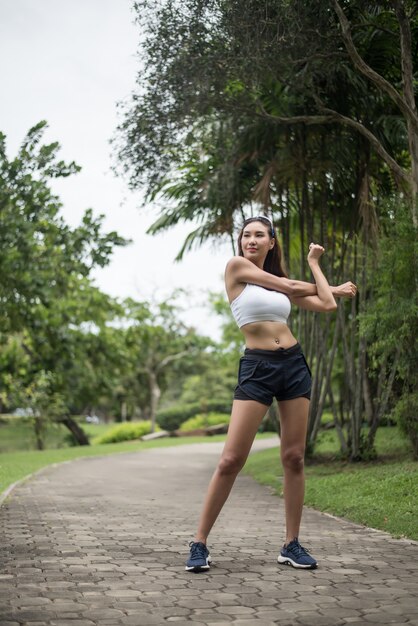 若いスポーツ女性ランナーは、公園でトラックを走る前に体を伸ばしています。