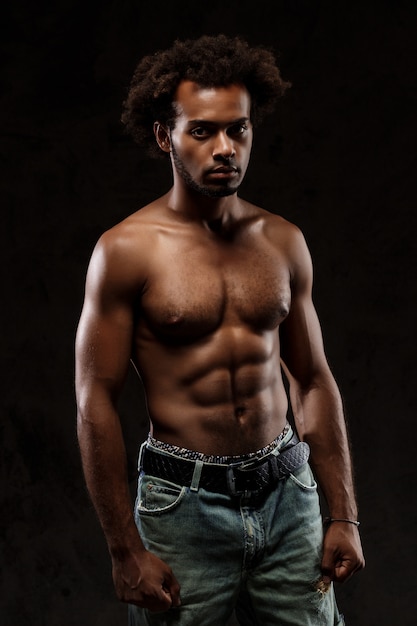 Young sportive african man posing over black wall.