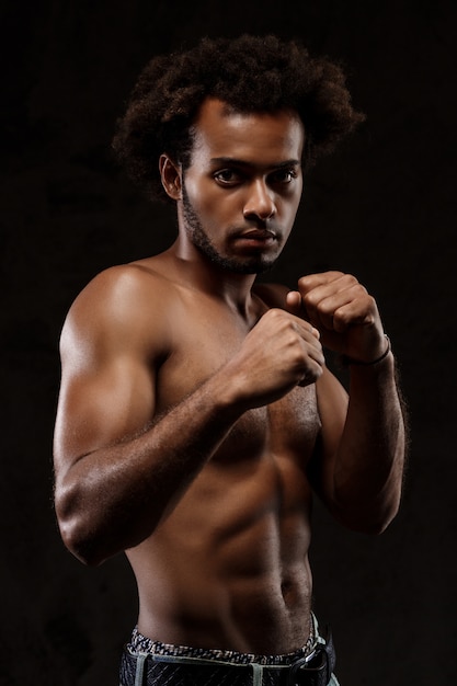 Young sportive african man posing over black wall.