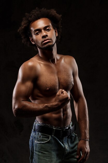 Young sportive african man posing over black wall.