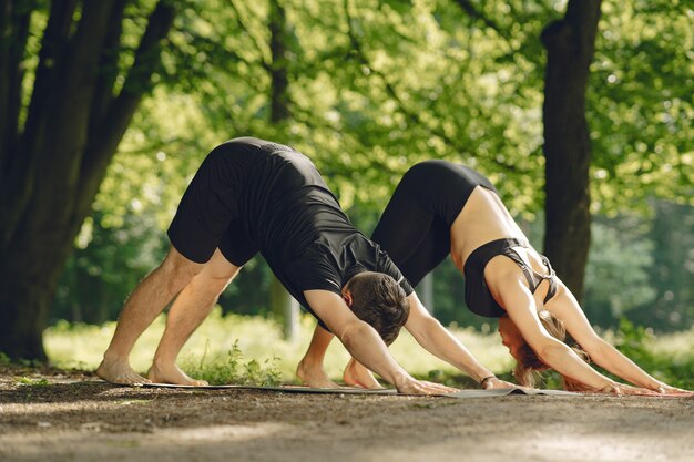 Young sportive couple doing yoga fitness . People in a summer park.