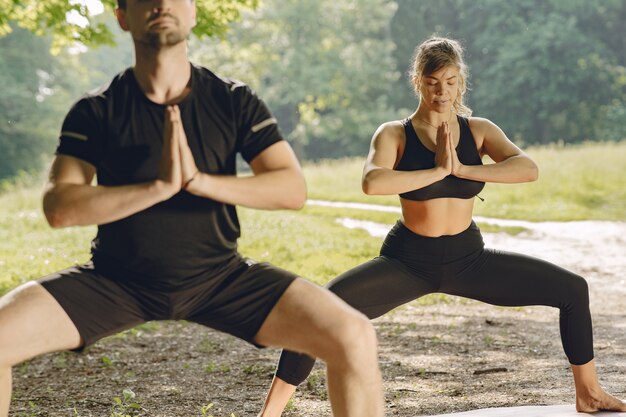 Young sportive couple doing yoga fitness . People in a summer park.