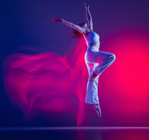 Young sportive girl in white stylish cloth dancing hiphop training isolated on purple bacground in neon