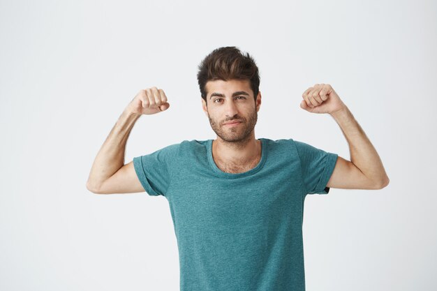 Молодой спортивный испанец парень в синей футболке и стильной прической, показывая играть с мышцами, позирует для фотосессии спортивного журнала.