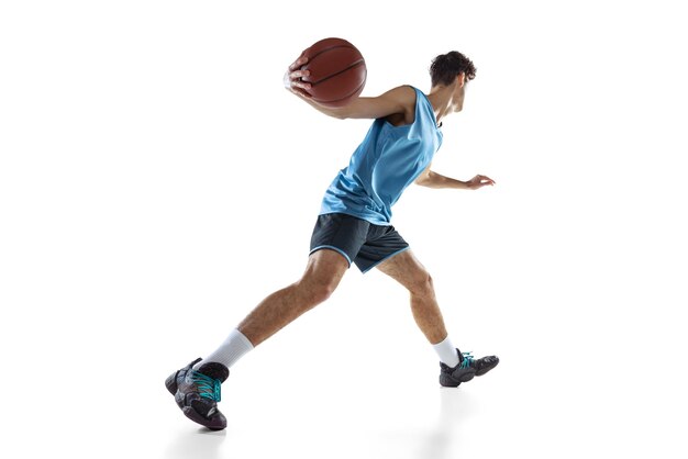 Young sportive man in blue uniform training basketball isolated on white. Side view