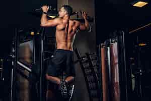 Free photo young sportive man is doing exercises for his back in dark gym club.