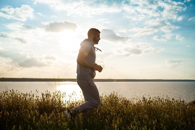 Young sportive man jogging in field at sunrise.