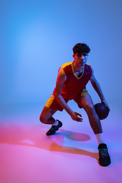 Бесплатное фото Молодой спортивный человек тренирует баскетбол, изолированный на градиенте в неоновом свете
