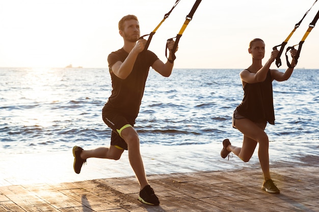 Young sportive people training with trx near sea in the morning.