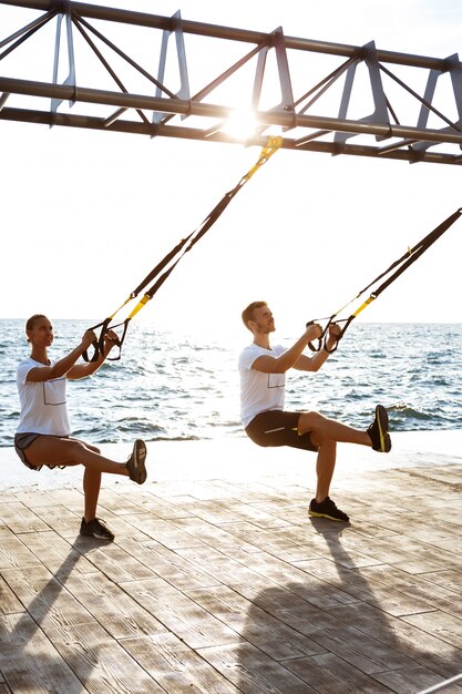 Young sportive people training with trx near sea in the morning.