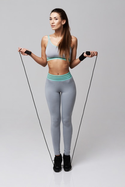 Young sportive woman doing exercises with jumping rope on white.