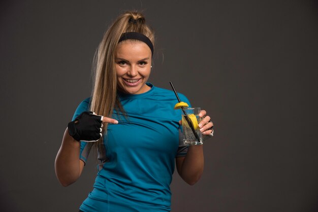 Young sportive woman having energy drink and pointing at it. 