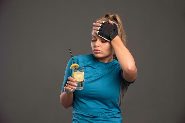 Молодая спортивная женщина устала и пьет воду с лимоном.