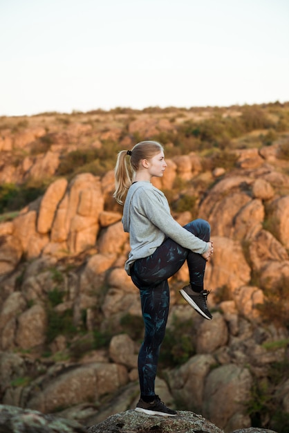 若い陽気な女性のトレーニング、峡谷の岩の上にストレッチ
