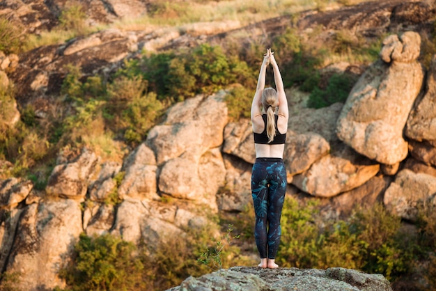 Young sportive woman training yoga asanas on rock in canyon