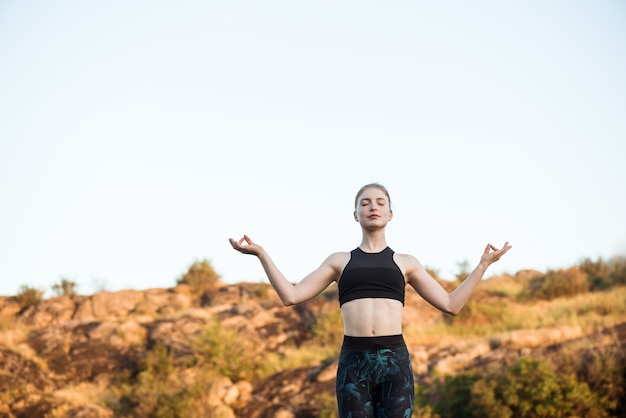 Молодая спортивная женщина, обучение асаны йоги на скале в каньоне
