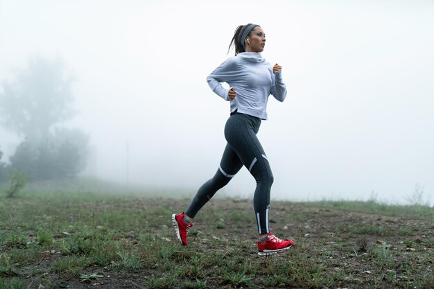 Free photo young sportswoman running along foggy field in nature copy space