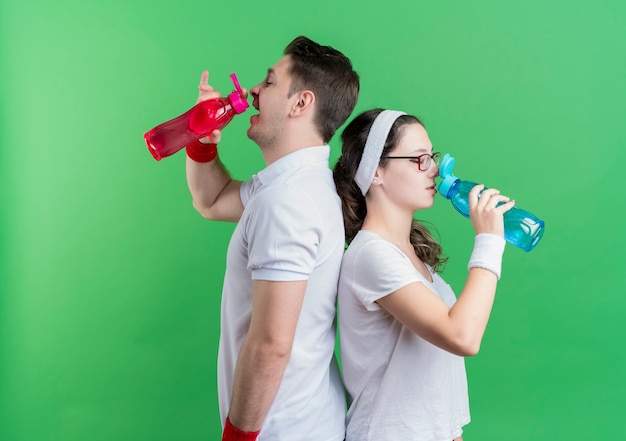 Young sporty couple drinking water after workout over green