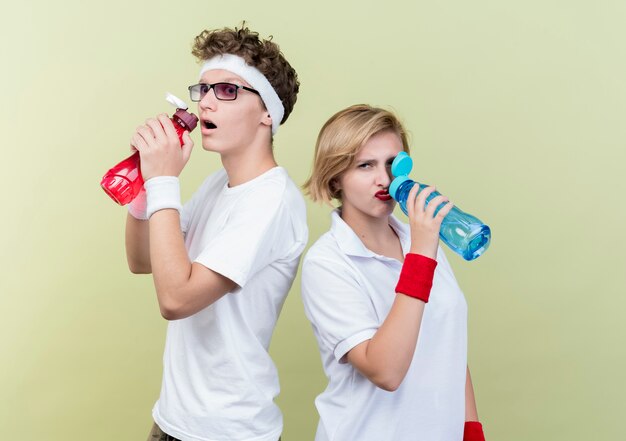 若いスポーティなカップルの男性と女性が軽い壁の上に立ってトレーニング後に水を飲む
