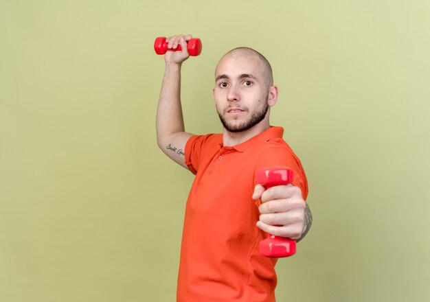 young sporty man exercising with dumbbells isolated on olive green wall