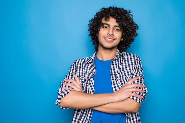 Young sporty man frowning face in displeasure, keeps arms folded against a blue wall