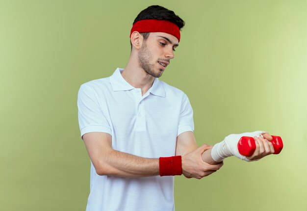 Giovane uomo sportivo in fascia che tocca il suo polso bendato sensazione di dolore sul verde