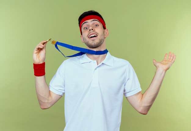 Free photo young sporty man in headband with gold medal around neck happy and excited over green