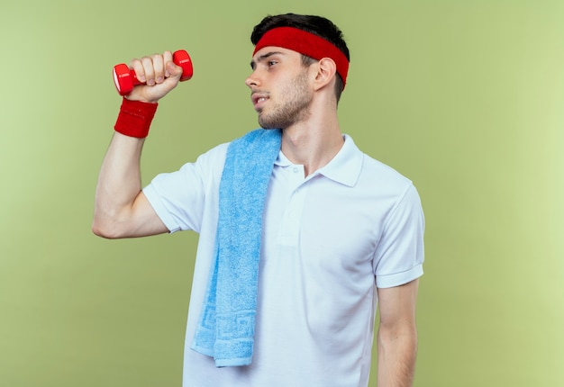 Free photo young sporty man in headband working out with dumbbell looking confident over green