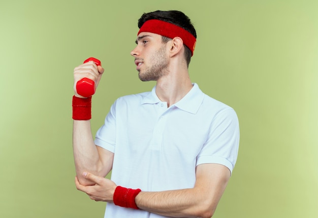 Free photo young sporty man in headband working out with dumbbell looking confident over green