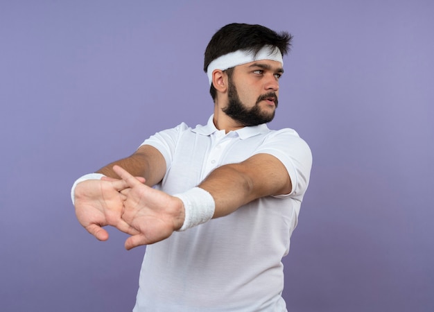 Foto gratuita giovane uomo sportivo guardando lato indossando la fascia e il braccialetto che allunga il braccio isolato sulla parete verde