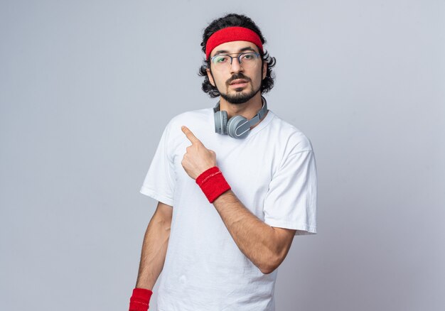 young sporty man wearing headband with wristband and headphones on neck points at side