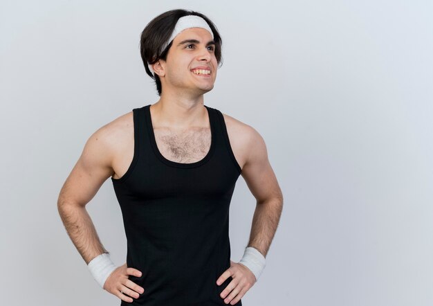 Free photo young sporty man wearing sportswear and headband looking aside smiling confident with arms at hip standing over white wall