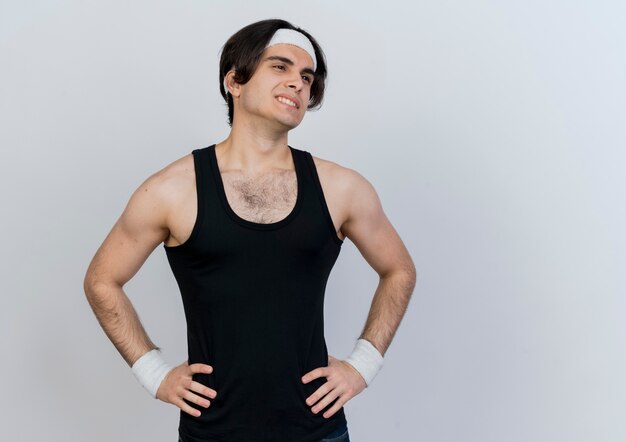 Young sporty man wearing sportswear and headband looking aside tired and bored standing over white wall