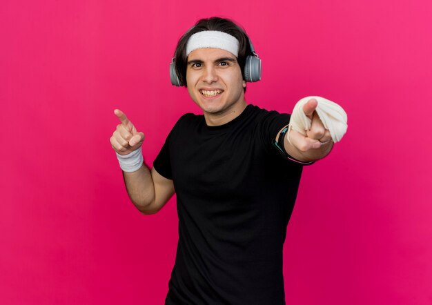 Young sporty man wearing sportswear and headband with heaphones and smartphone armband pointing at camera strained and confident 