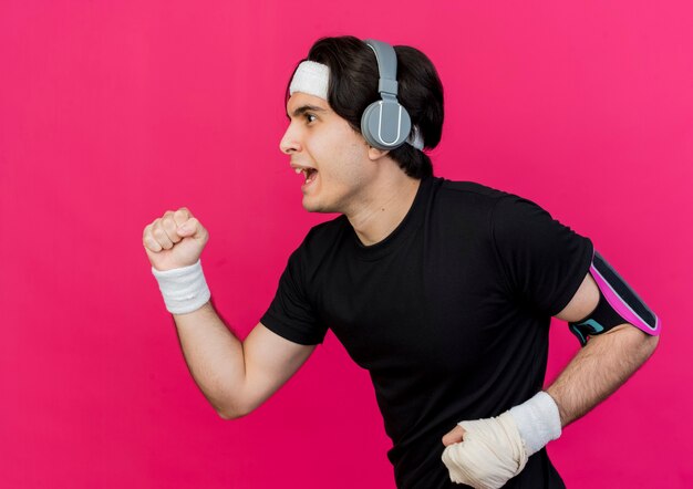 Young sporty man wearing sportswear and headband with heaphones and smartphone armband working out hard 