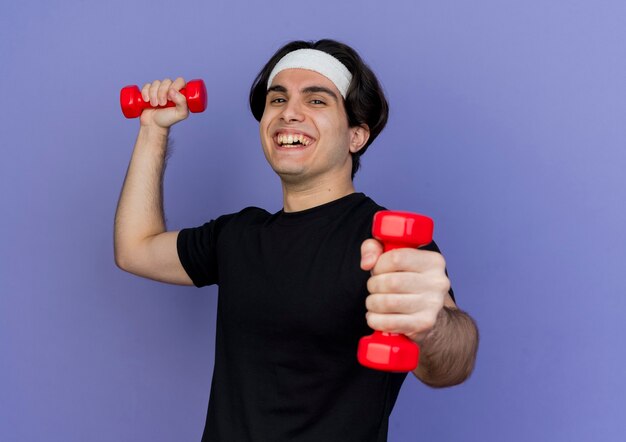 Young sporty man wearing sportswear and headband working out with dumbbells smiling cheerfully with happy face 