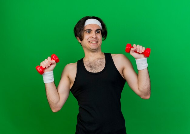 Young sporty man wearing sportswear and headband working out with dumbbells smiling cheerfully 