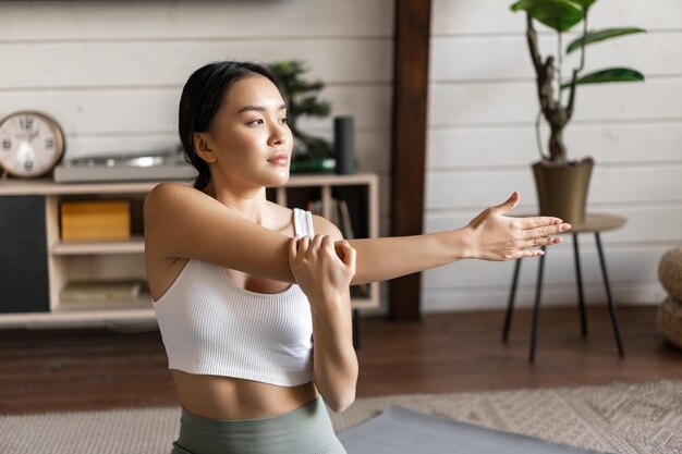 Young sporty woman in activewear doing stretching morning yoga or workout at home sitting on floor mat