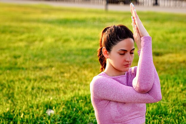 Young sporty woman practicing yoga in a pink yoga suit at sunrise in the park